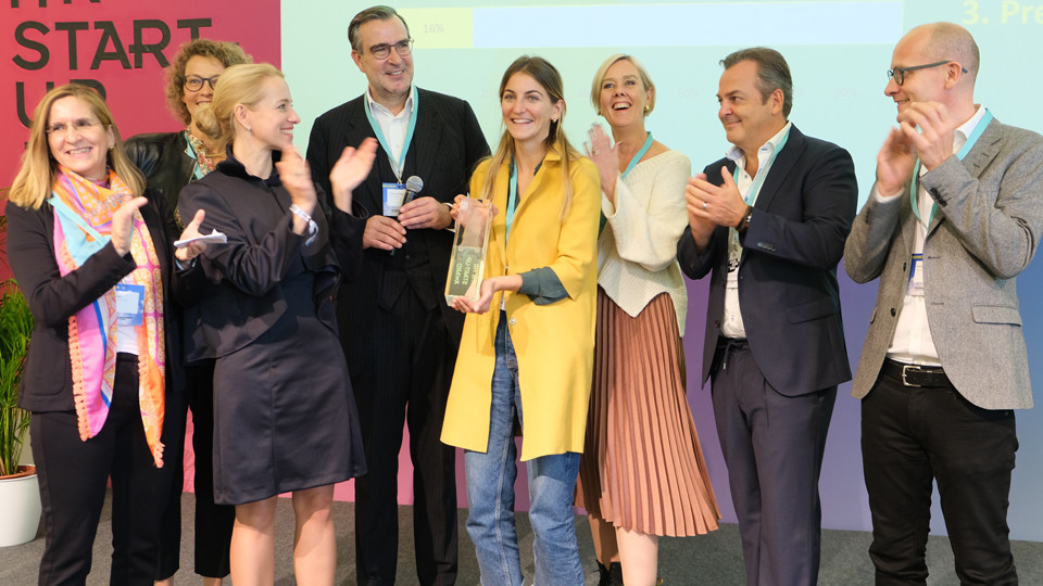 Lara von Petersdorff-Campen from evermood stands happily on stage with the award in her hands and surrounded by jury members.