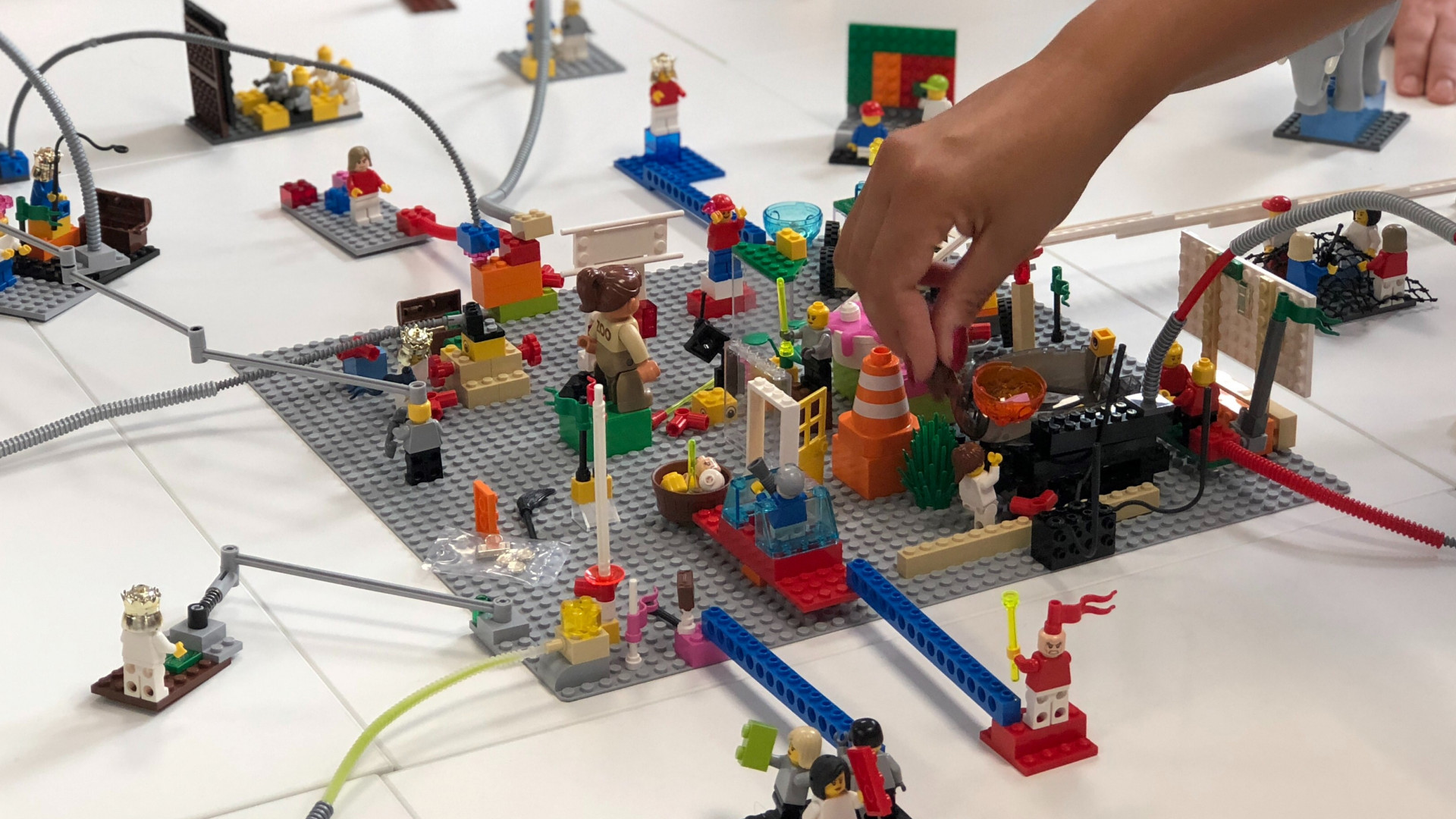 Eine Hand greift nach einer Lego-Figur, die sich auf einer Platte mit unterschiedlichen Aufbauten und Figuren befindet.